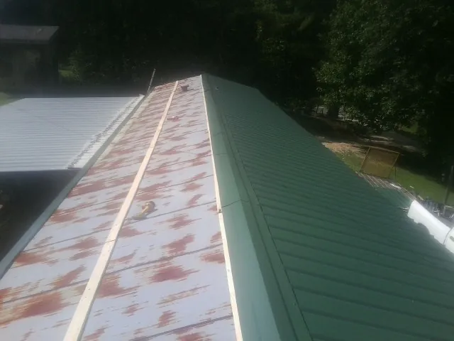 Old rusted panels beside newly installed green metal roofing — Wind Damage Roof Repair by Roofing Brothers in Riverdale