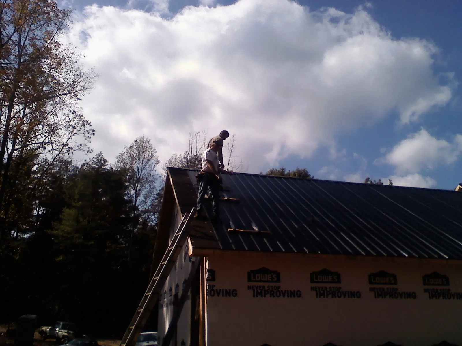 Roofer fastening dark metal panels high against a cloudy sky, from a Roof Inspection job in Riverdale