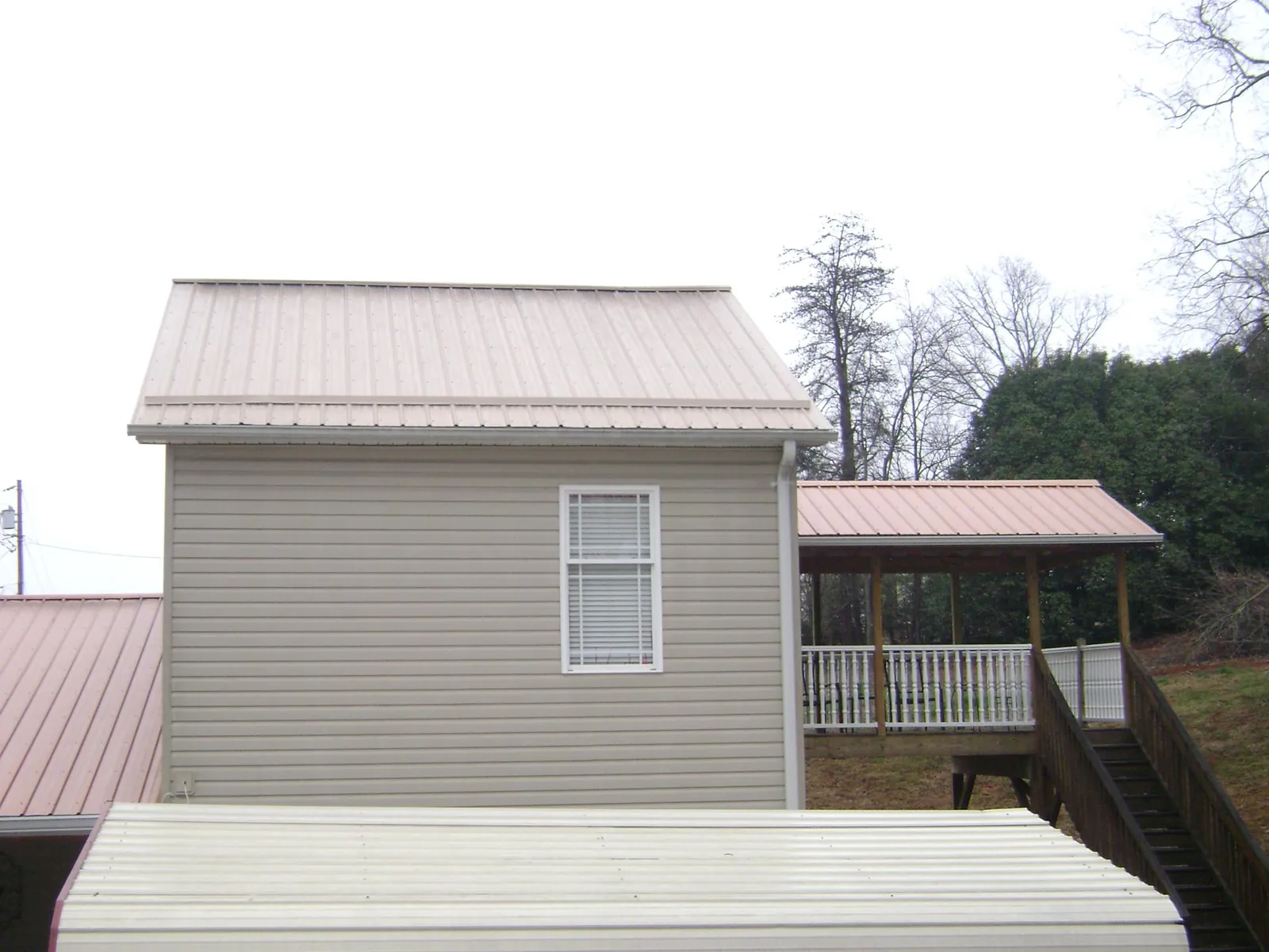 Tan metal roofs on a two story addition and attached porch, from a Roof Replacement job in Riverdale
